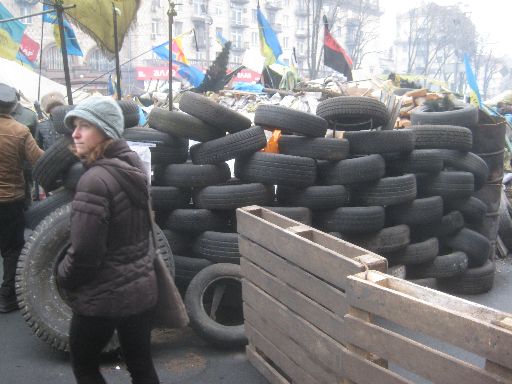 A barricade of tires and shipping planks, with both the official and alternative Ukrainian flags overhead