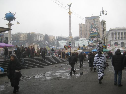 Another view of the main protest area with booths, flags, Euromaidan 'Christmas tree,' and person in zebra costume.