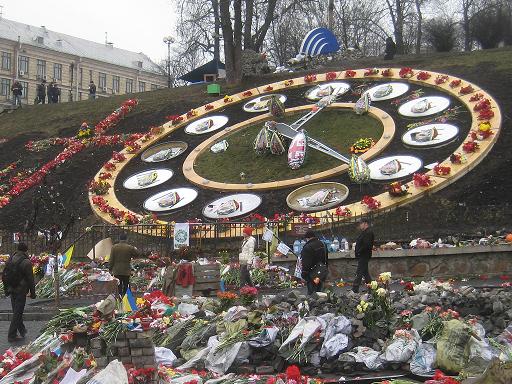 The memorials on, in front of, and beside the clock on Instytutska Street.  Many flower arrangements are in the colors of the Ukrainian flag, and one in the center is in the design of the flag of Georgia, the country Russia last invaded before invading Crimea.